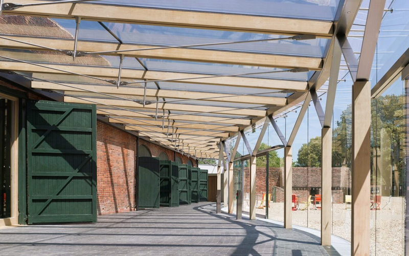 glass roof with timber beams in a modern glass canopy with wooden beams and exposed brick walls.